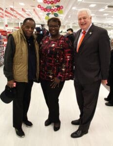 Three people standing in a store with one man wearing an orange tie.