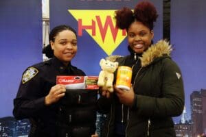 Two women holding up items in front of a yellow and blue sign.