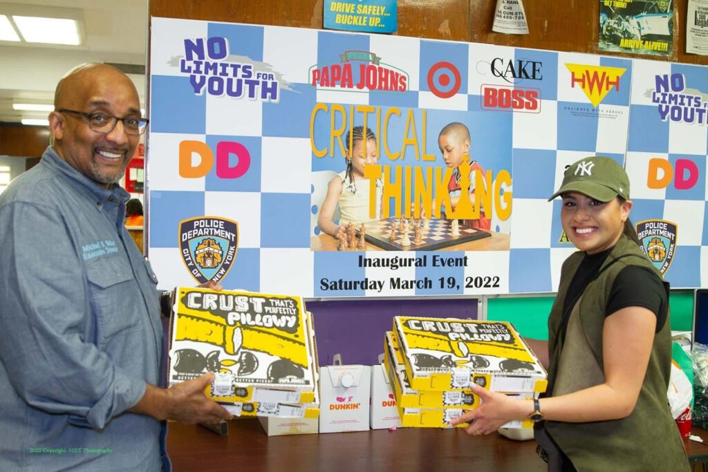 Two men holding boxes of pizza in front of a poster.